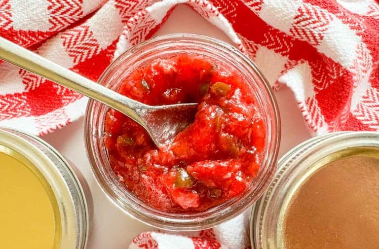 Homemade strawberry jam in a glass jar with a spoon, ready to spread on bread.