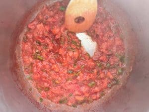 Strawberry and jalapeño mixture simmering in a pot with a wooden spoon, steam rising.