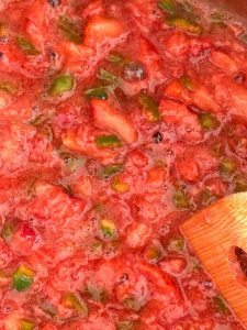 Close-up of bubbling jam mixture with visible pieces of strawberries and green jalapeños.
