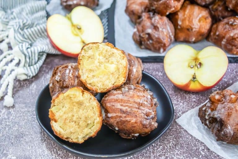 Plate of fritters with two cut in half to display the apple-filled inside.
