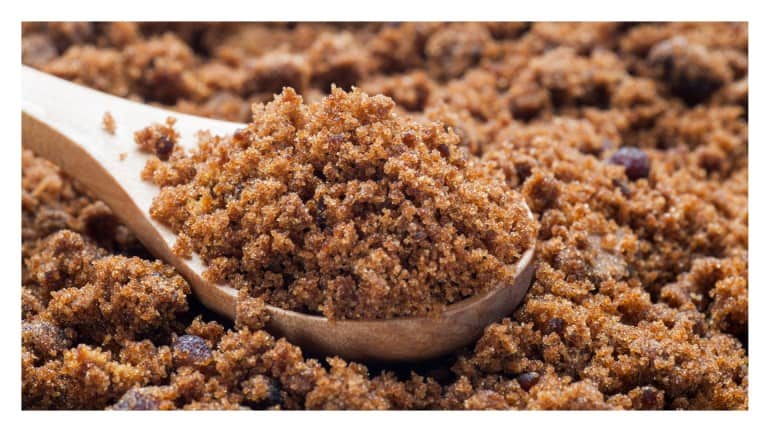 Wooden spoon heaped with moist, dark brown sugar surrounded by more brown sugar.