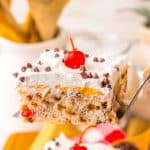 A slice of chocolate cherry poke cake being lifted with a server, showing layers and topping clearly.