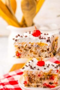 A slice of chocolate cherry poke cake being lifted with a server, showing layers and topping clearly.