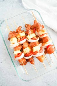 Glass dish filled with assembled uncooked chicken teriyaki skewers.
