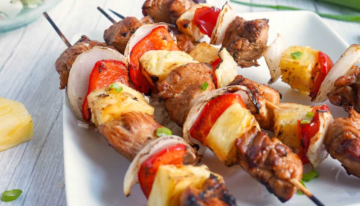 Grilled chicken teriyaki skewers with pineapple, onion, and red pepper served on a white plate.