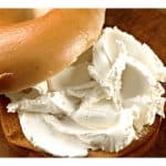 Bagel spread with a thick layer of cream cheese on a wooden surface.