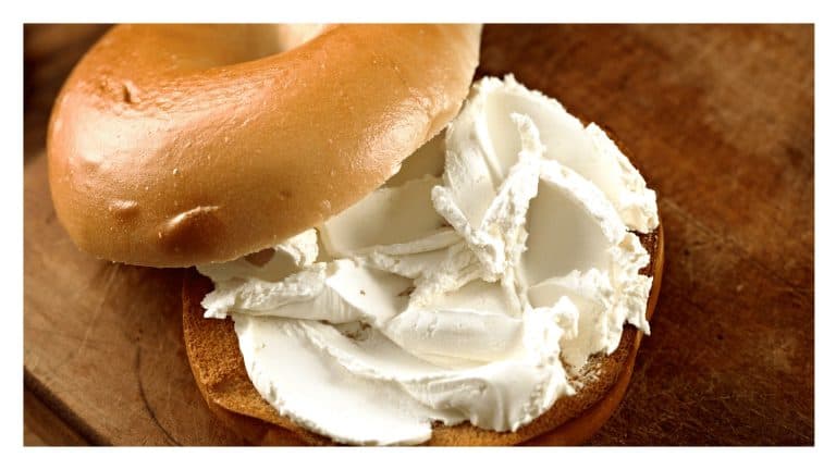 Bagel spread with a thick layer of cream cheese on a wooden surface.