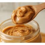 Wooden spoon scooping creamy peanut butter.