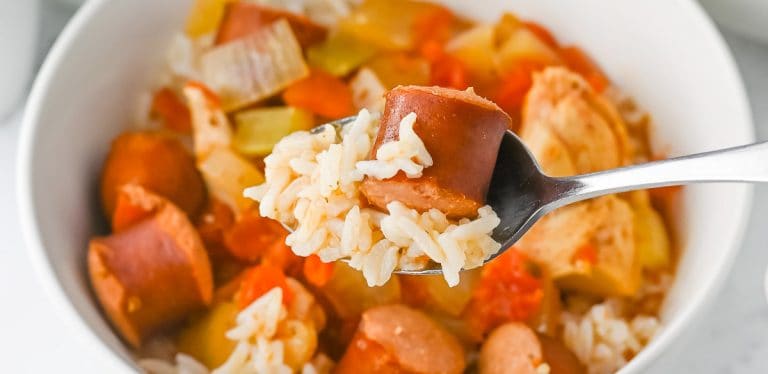 Spoon holding sausage and rice over a bowl of jambalaya.