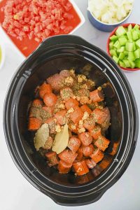 Crock pot filled with sausage, garlic, spices, and bay leaves.