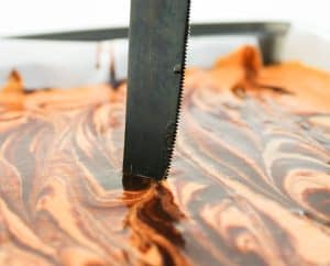 Close-up of swirling chocolate and pumpkin layers with a knife.