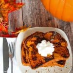 Pumpkin French toast on a plate with whipped cream and a large pumpkin nearby.