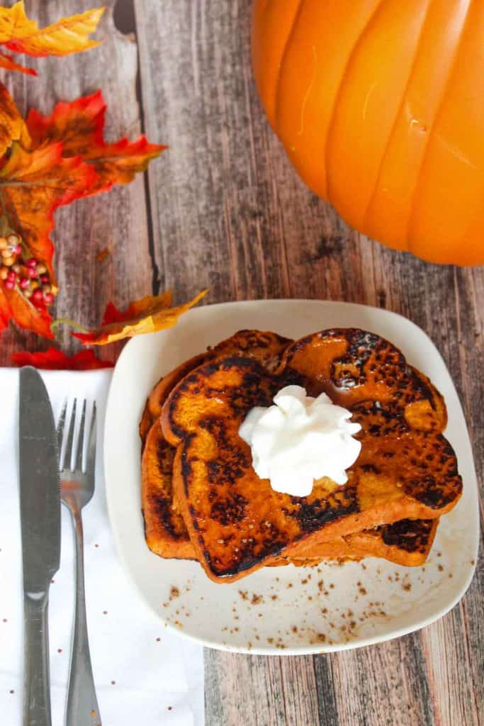 Pumpkin French toast on a plate with whipped cream and a large pumpkin nearby.