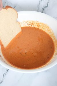 Slice of bread being dipped into the pumpkin mixture.