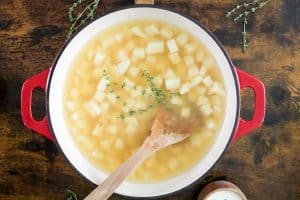 Diced potatoes and broth with thyme in a red pot.