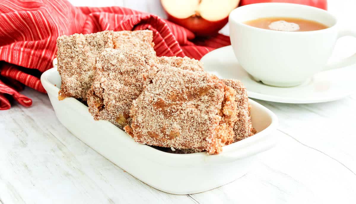 Apple cider blondies in a dish with a cup of tea in the background.