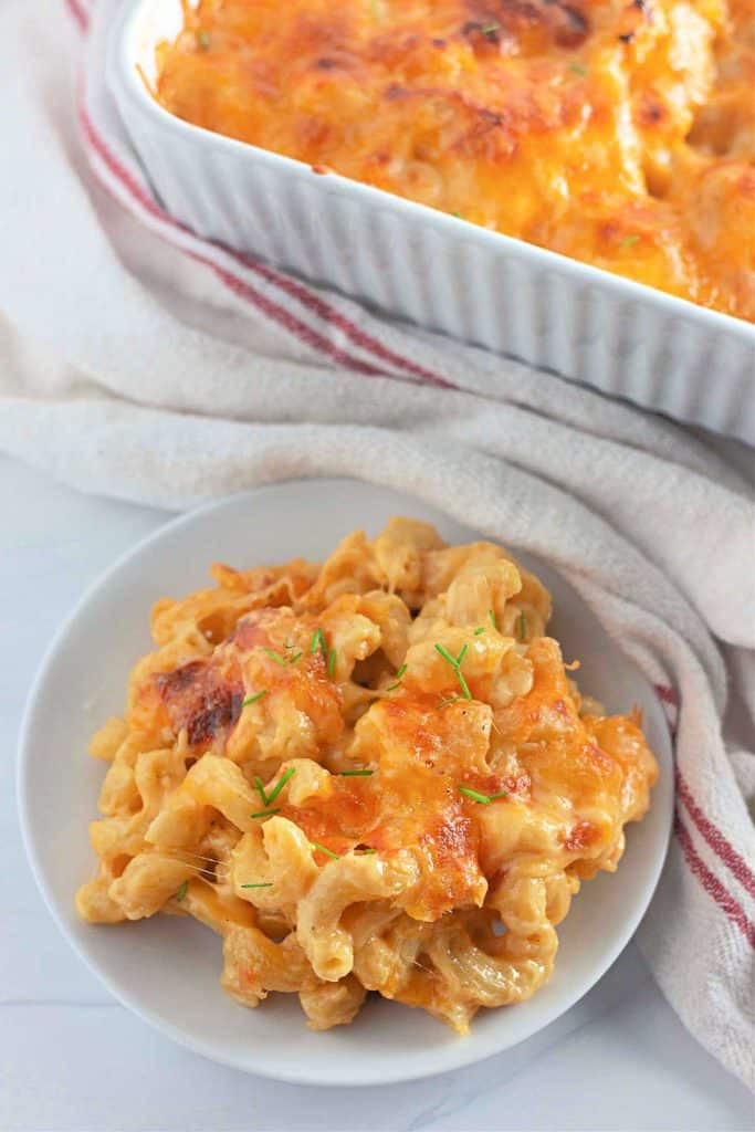 Casserole dish of baked macaroni and cheese with serving on plate.