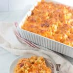 Casserole dish of baked macaroni and cheese with serving on plate.
