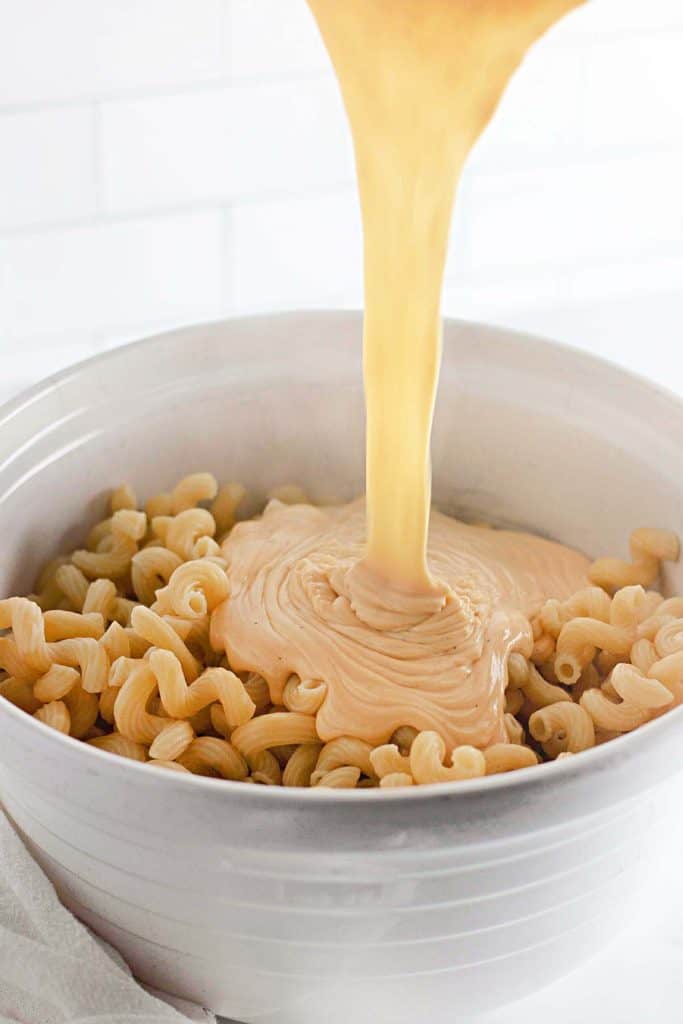 Close-up of cheese sauce pouring onto pasta in a bowl.