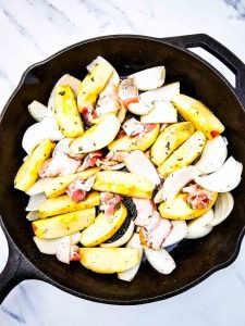 Apples, onions, and bacon seasoned and ready to cook in a cast iron skillet.