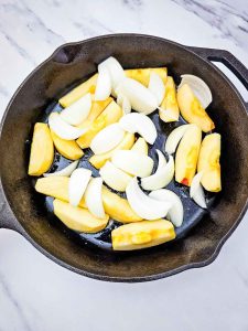 Apples and onions added to a cast iron skillet.