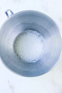 Foamy egg whites starting to whip in a mixing bowl.