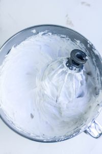 Thick white meringue forming in a mixer bowl.