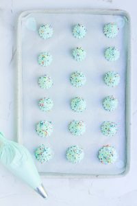 Green meringue piped onto a baking sheet with sprinkles.