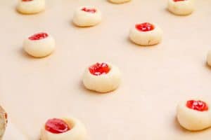 Jam-filled thumbprint cookies arranged on a baking sheet.