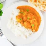 Plate of butter chicken with white rice, garnished with cilantro and served beside naan bread.
