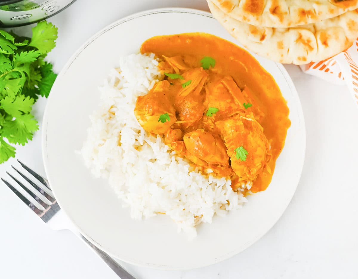 Plate of crock pot butter chicken served with white rice and naan bread.