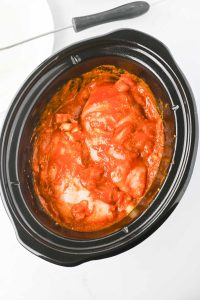 Raw chicken breasts in butter chicken sauce inside a slow cooker.