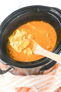 Plate of butter chicken and rice with naan bread and a slow cooker in the background.