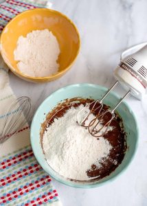 Flour added to chocolate batter in a teal bowl.