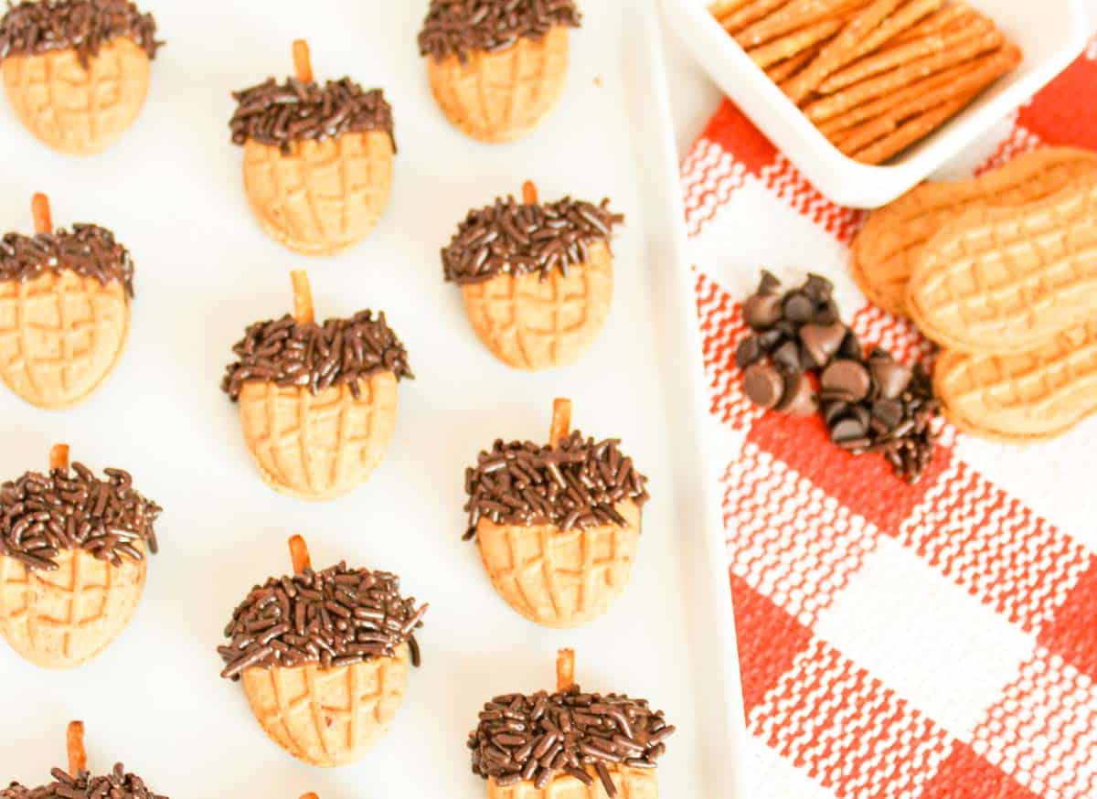 Nutter Butter acorn cookies topped with chocolate sprinkles and pretzel stems on a tray.