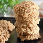 Stack of peanut butter no-bake cookies on a black tray with more cookies in the background.