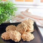 Pile of peanut butter no-bake cookies on a black tray near a plant and towel.