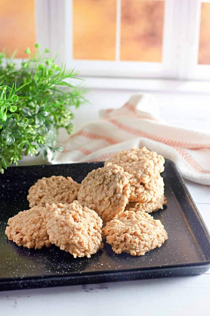 Pile of peanut butter no-bake cookies on a black tray near a plant and towel.