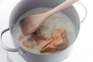 Peanut butter added to melted butter and sugar mixture in a saucepan with a wooden spoon.