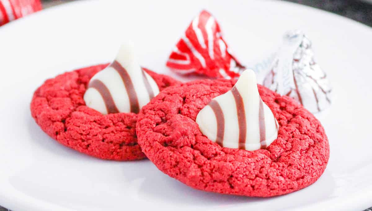 Two red velvet blossom cookies with striped kisses on a white plate.