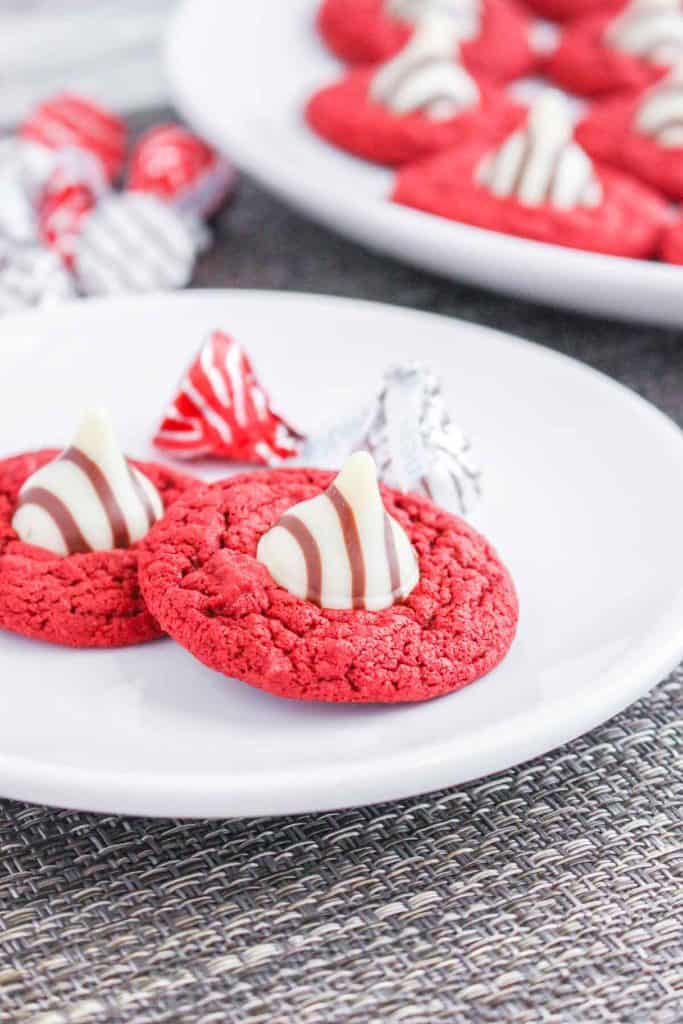 Two red velvet blossom cookies with striped kisses on a white plate.