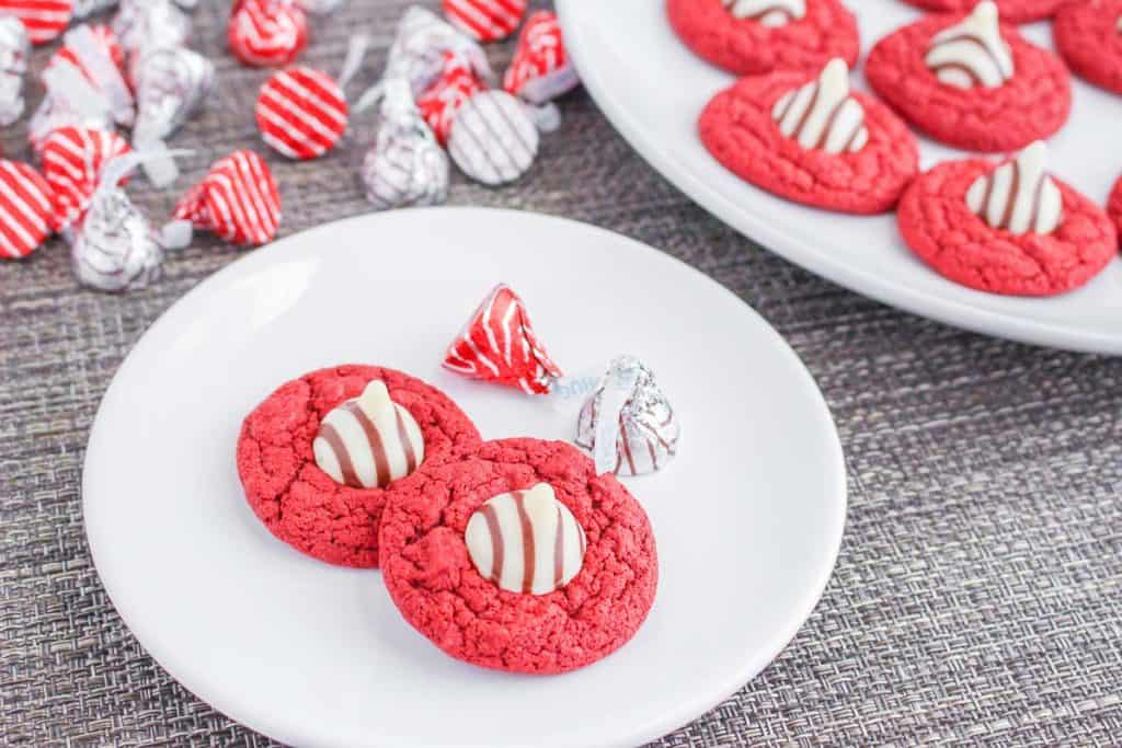 Red velvet blossom cookies served on a white plate with wrapped chocolates in the background.