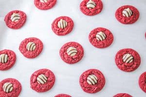 Rows of red velvet blossom cookies cooling on parchment paper.