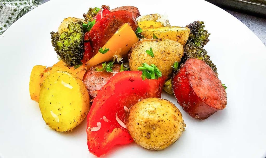Close-up of roasted sausage, potatoes, and peppers garnished with parsley.