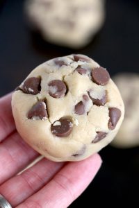 Cookie dough ball held in hand showing chocolate chips.