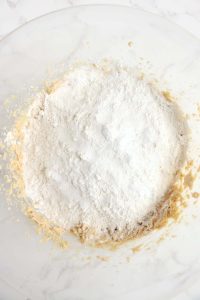 Flour added to the wet cookie mixture in a bowl.