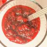 Finished brown sugar cranberry sauce in a glass bowl with a serving spoon.