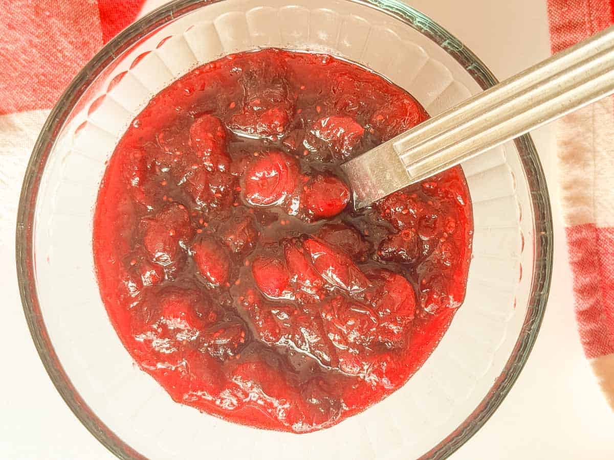 Finished brown sugar cranberry sauce in a glass bowl with a serving spoon.