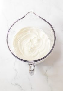 Finished whipped cream in a glass measuring cup.