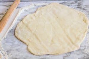 Dough rolled flat with a rolling pin on a floured surface.